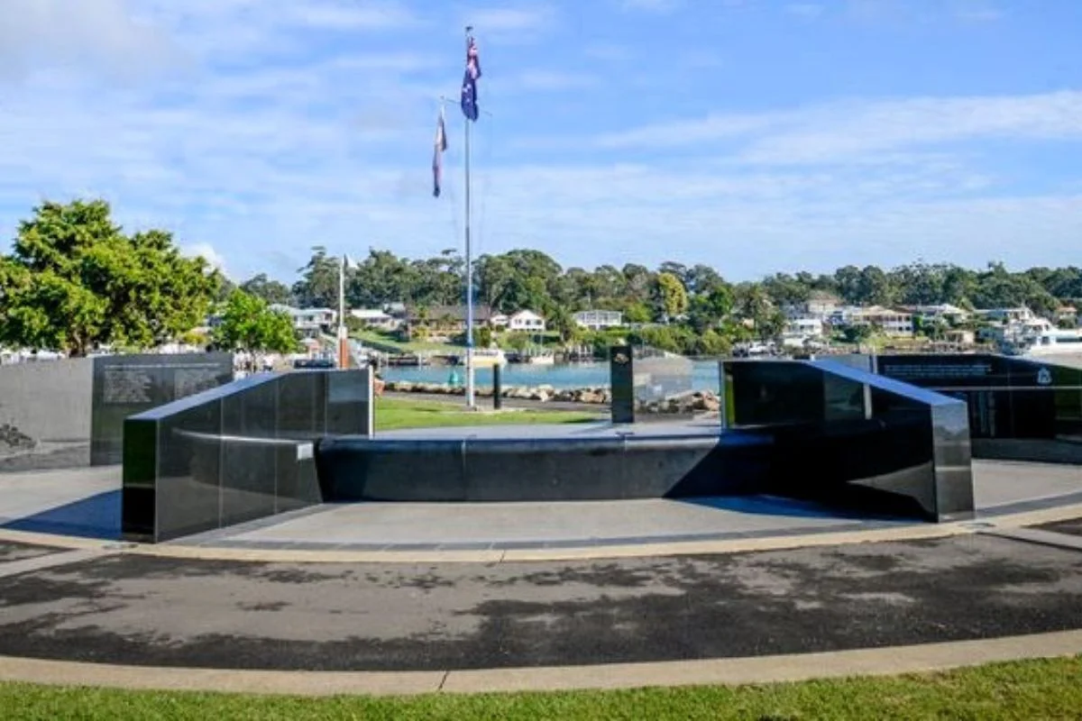 Coastal memorial plaza with black stone walls and central flagpole