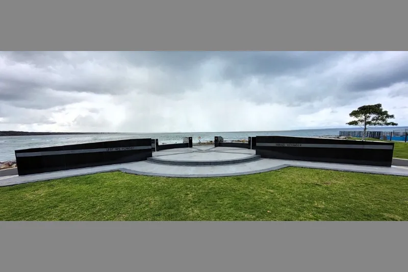 Wide view of the memorial site by the water under cloudy skies.