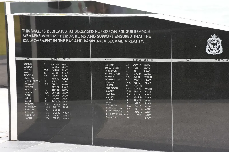 Close-up of engraved names and service details on a black memorial wall.
