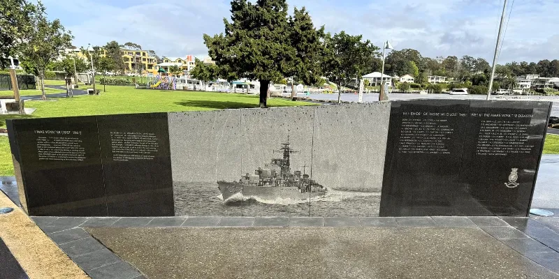 Stone memorial wall featuring an engraved image of a naval ship and commemorative text.