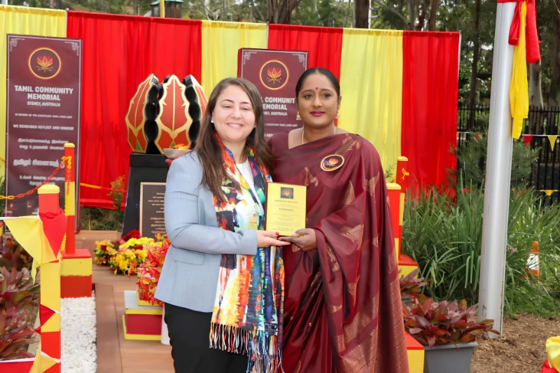Two women holding a recognition plaque at the Tamil Community Memorial in Sydney.