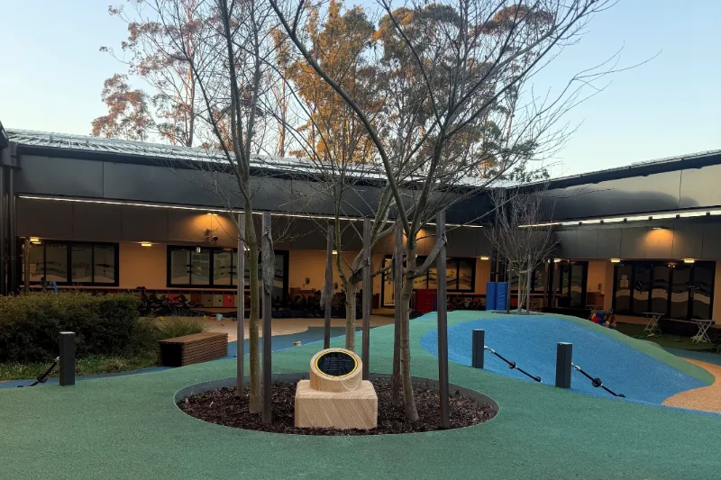 Sandstone memorial plinth with commemorative plaque installed among trees in the NextSense School playground.