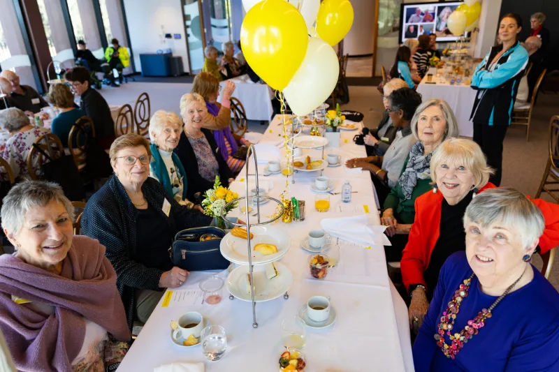 Lantern Club members enjoying afternoon tea with yellow and white balloons at NextSense.